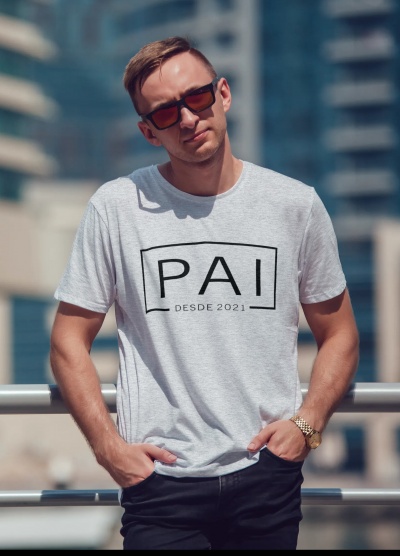 Homem com t-shirt cinza claro escrita PAI DESDE 2021 e óculos escuros em ambiente urbano