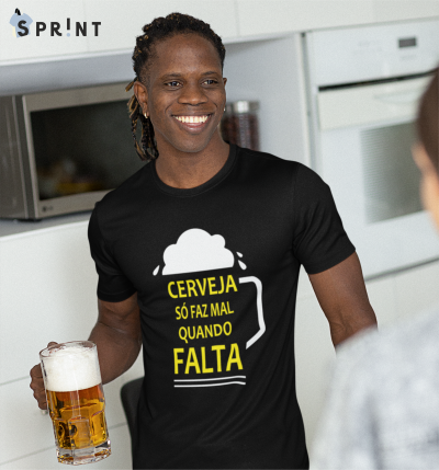 Homem a usar camiseta preta com estampa de cerveja e texto, segurando caneca de cerveja numa cozinha.