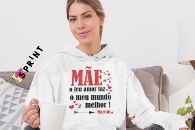 Mulher jovem com sweatshirt branca com texto para mãe segurando caneca branca num ambiente interior confortável.