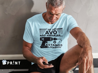 Homem de t-shirt azul clara com texto e imagens de ferramentas sentado junto a uma parede cinzenta