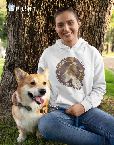 Pessoa com hoodie branco com estampa de cão junto a um cão Corgi em parque