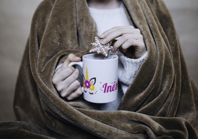 Caneca branca com nome Inês e flores segurada por mãos, mergulhando biscoito estrela decorado, com cobertor castanho