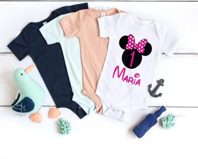 Quatro bodies de bebé de várias cores com brinquedos e decoração num fundo branco