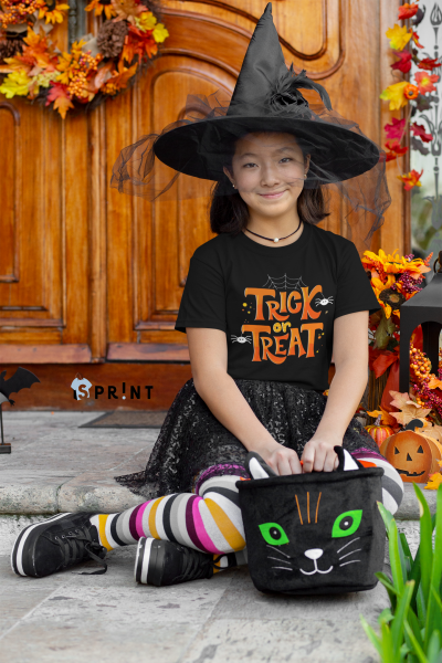 Criança fantasiada de bruxa com mochila de gato e t-shirt 'TRICK or TREAT' sentada em degrau com decoração Halloween