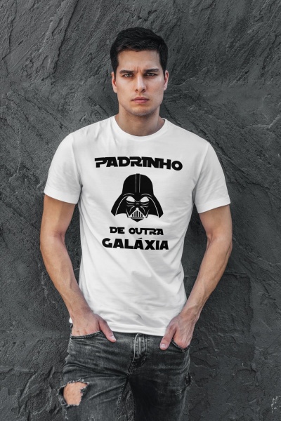 Homem com t-shirt branca com texto e imagem do Darth Vader frente à parede cinzenta