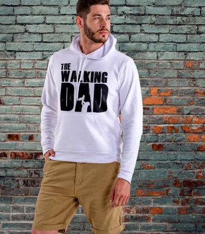 Homem com suéter branco estampado THE WALKING DAD e calções bege em frente a parede de tijolos