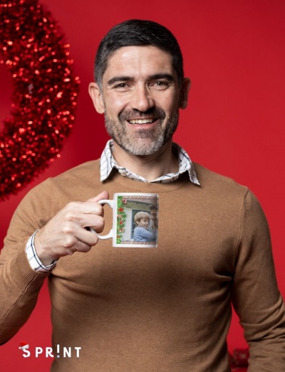 Homem a sorrir segurando uma caneca com foto e decoração natalícia, fundo vermelho