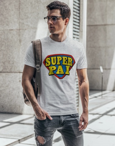 Homem vestido com camiseta cinza clara com estampa SUPER PAI, jeans rasgados cinza e mochila castanha em ambiente urbano