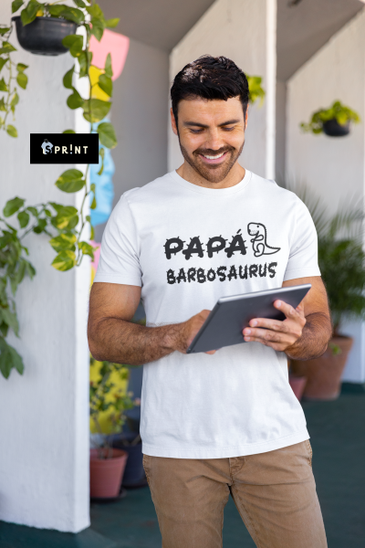 Homem com t-shirt branca com texto e desenho de dinossauro lendo tablet