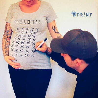 Mulher grávida a usar camisola cinzenta com texto e contagem régua, homem a riscar números com marcador