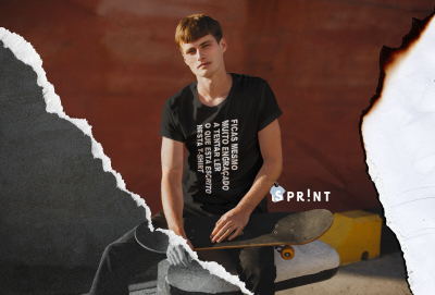 Homem jovem com t-shirt preta e skate sentado num muro amarelo sob fundo vermelho