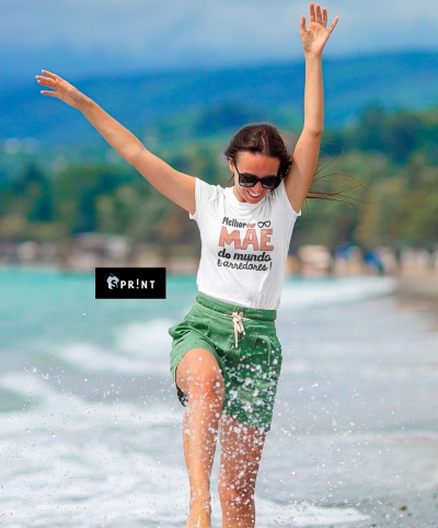 Mulher com t-shirt branca com texto e calções verdes brincando na praia
