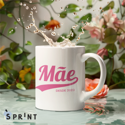 Caneca branca com texto rosa Mãe DESDE 2023, líquido a salpicar, fundo de plantas e flores