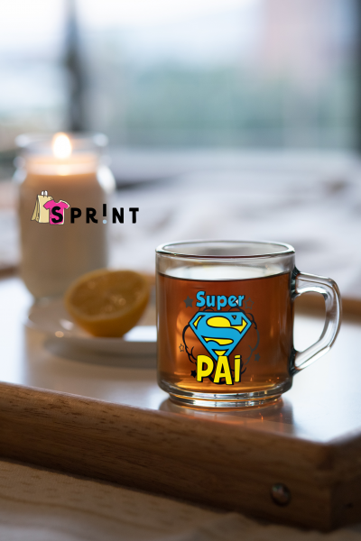 Caneca de chá com texto Super PÁI em vidro sobre uma bandeja de madeira com limão e vela ao fundo