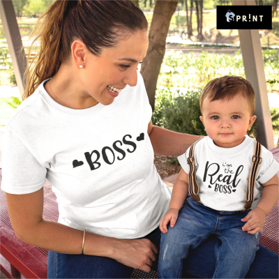 Mulher e bebé com camisolas brancas com texto preto sentados numa mesa de piquenique ao ar livre