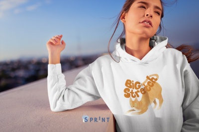 Mulher com sweatshirt branca e estampa amarela de cão e texto 'Big Stretch' contemplando o horizonte ao ar livre.