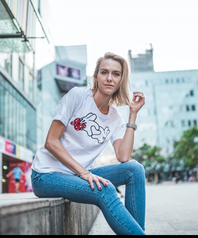 Mulher sentada usando t-shirt branca com estampa de coelho e jeans azuis numa rua urbana.