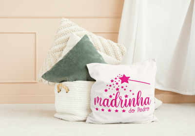 Almofada branca com texto e desenhos rosa junto a cesta com almofadas num ambiente claro