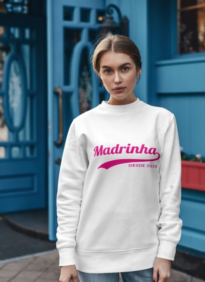 Mulher veste sweatshirt branca com texto rosa 'Madrinha DESDE 2020' em frente a porta azul