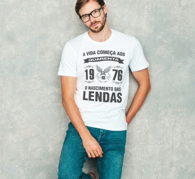 Homem com t-shirt branca e calças de ganga azuis junto a parede cinzenta.