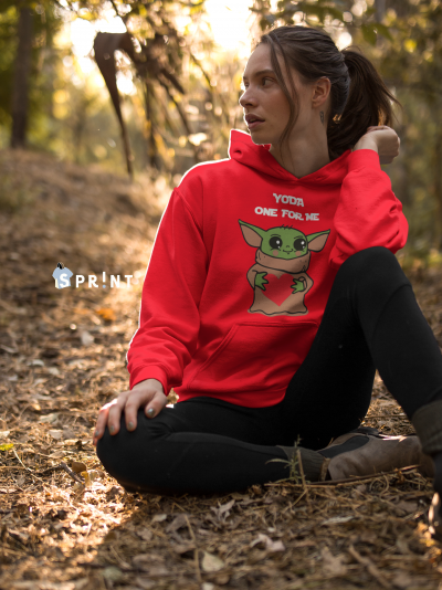 Mulher sentada no chão de floresta com hoodie vermelho 'YODA ONE FOR ME' e calças pretas