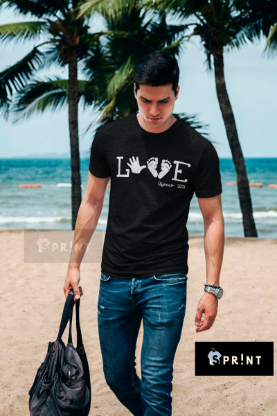 Homem na praia com camiseta preta LOVE, texto Afonso 2021, segurando mala preta.