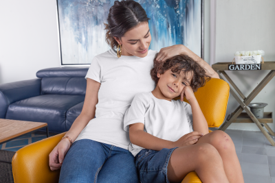 Mulher e criança com camisetas brancas sentados numa cadeira laranja num ambiente interior com sofá azul e placa 'GARDEN'