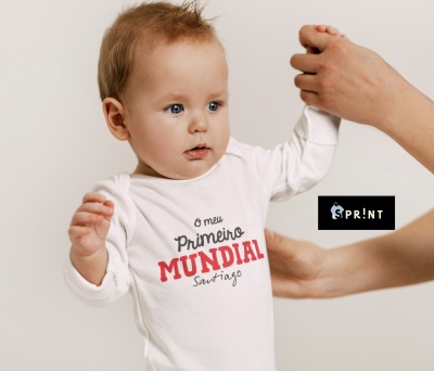 Body branco de bebé com texto 'O meu Primeiro MUNDIAL Santiago' e mãos adultas a segurá-lo