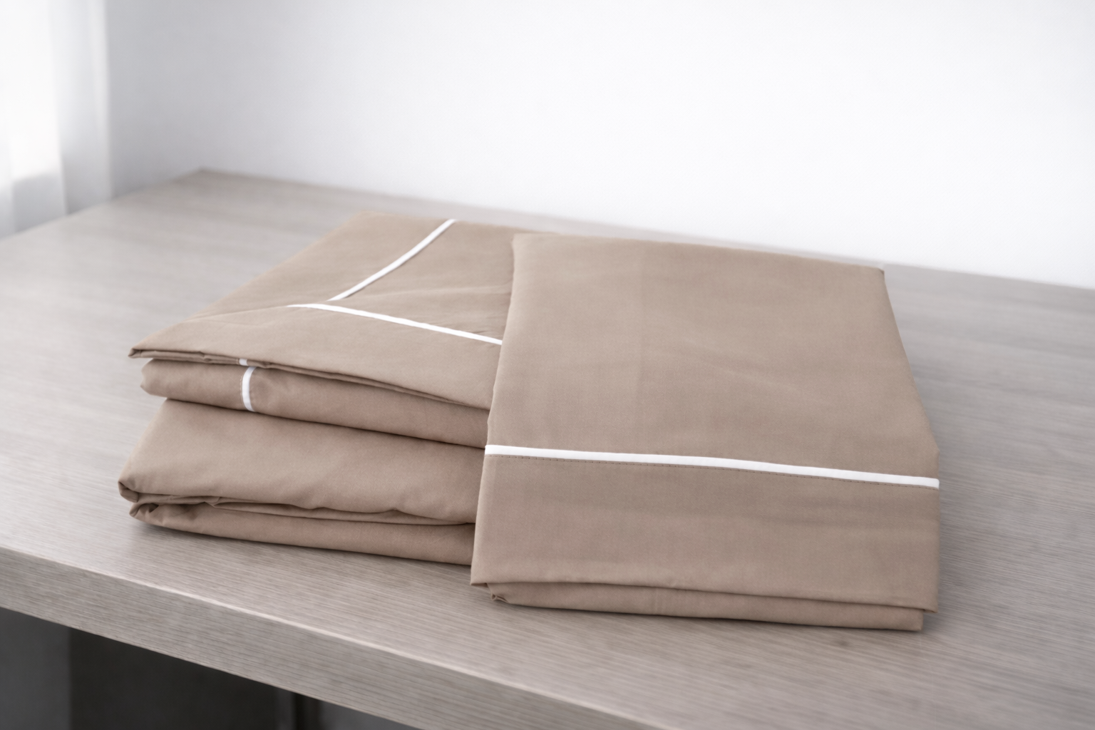 Conjunto de roupa de cama bege com detalhes brancos dobrado sobre mesa de madeira.