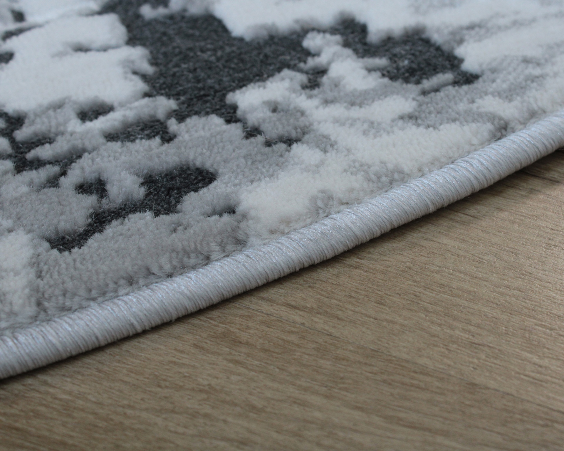 Tapete felpudo cinza e branco com padrão abstrato e borda romana