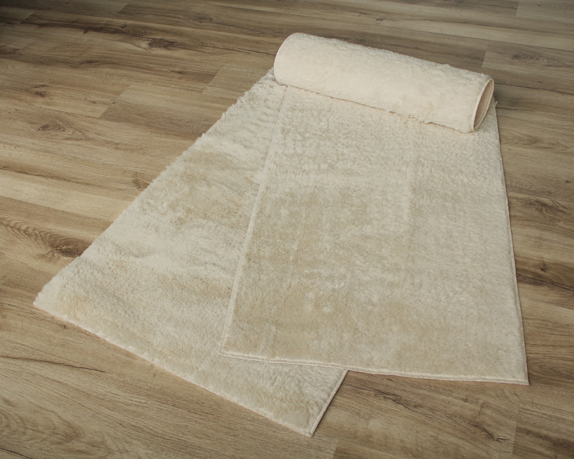 Tapete branco felpudo parcialmente enrolado sobre chão de madeira clara