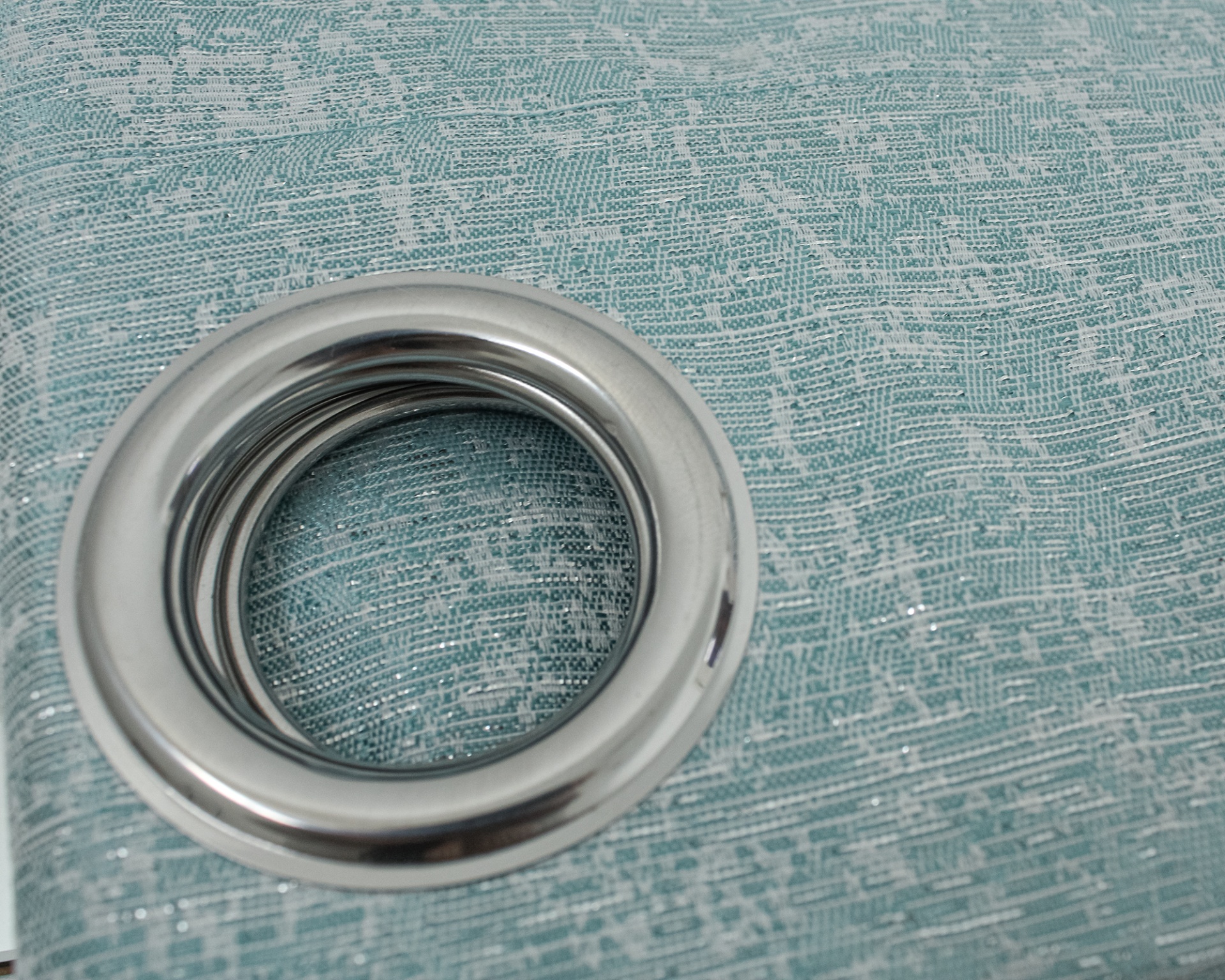 Argola metálica prateada sobre tecido azul com padrão texturizado