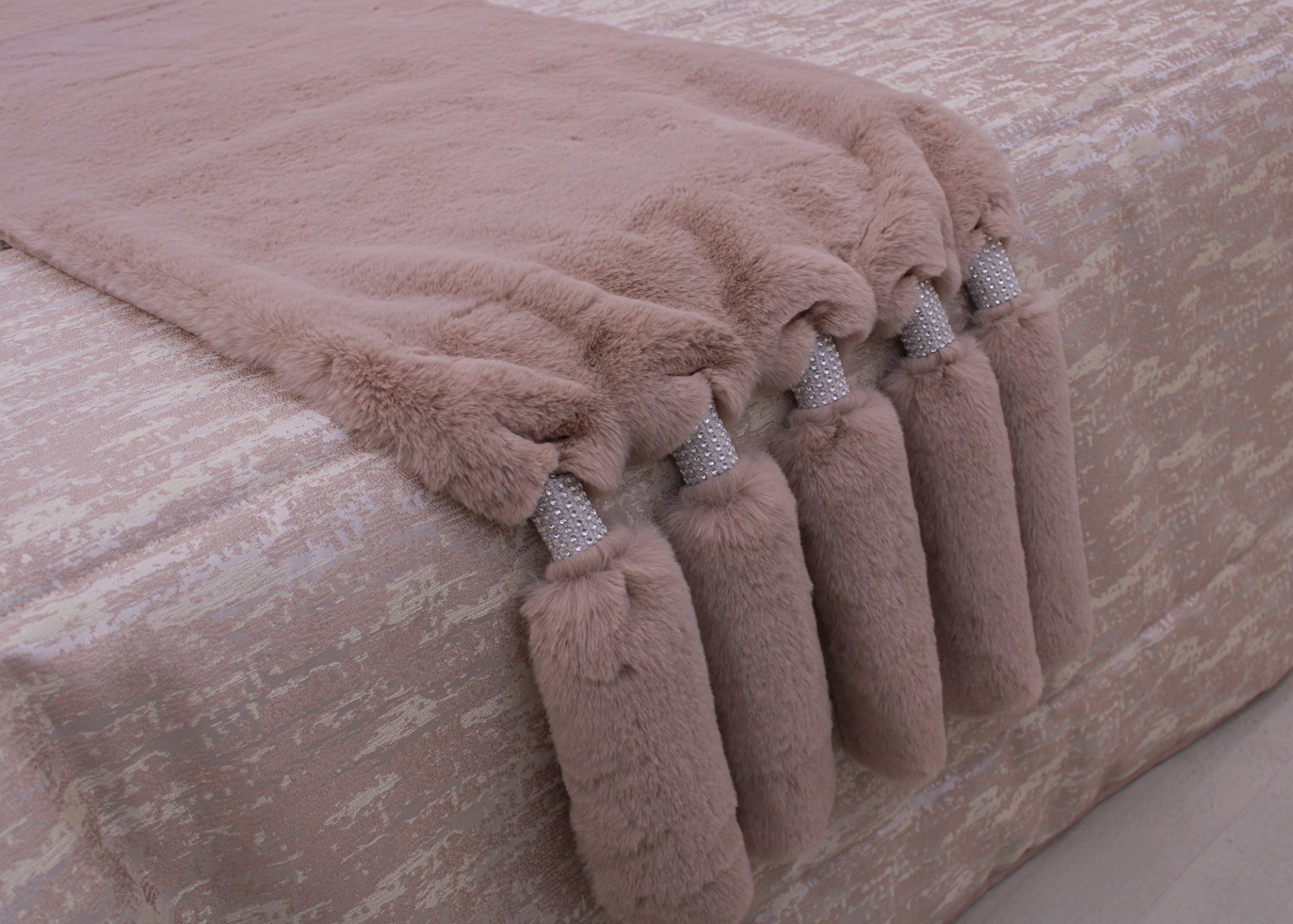 Manta felpuda rosa clara com tasséis decorativos sobre tecido com padrão rosa e bege