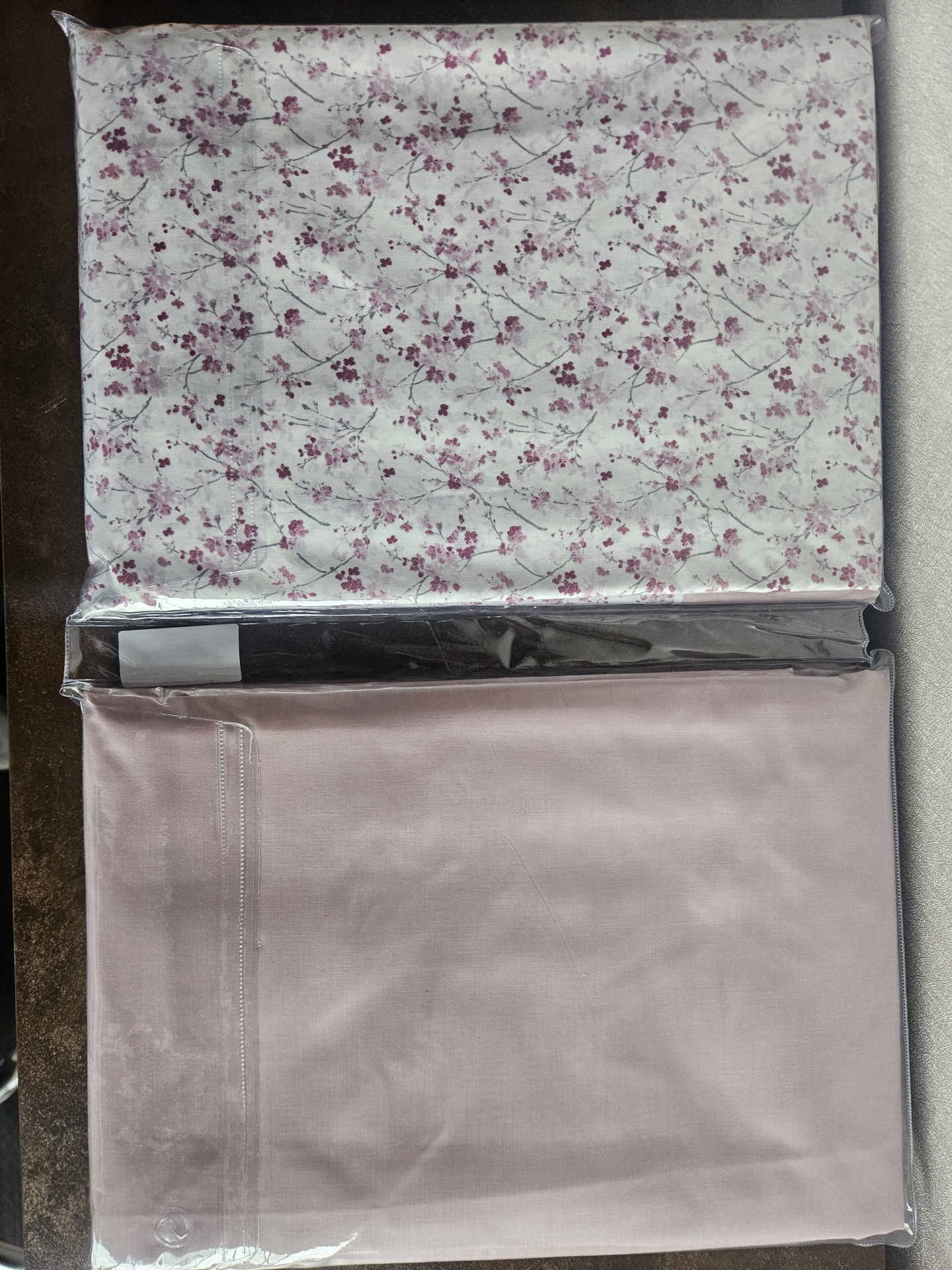 Tecidos dobrados embalados em plástico, um com padrão floral e dois lisos em tons rosa e escuro.