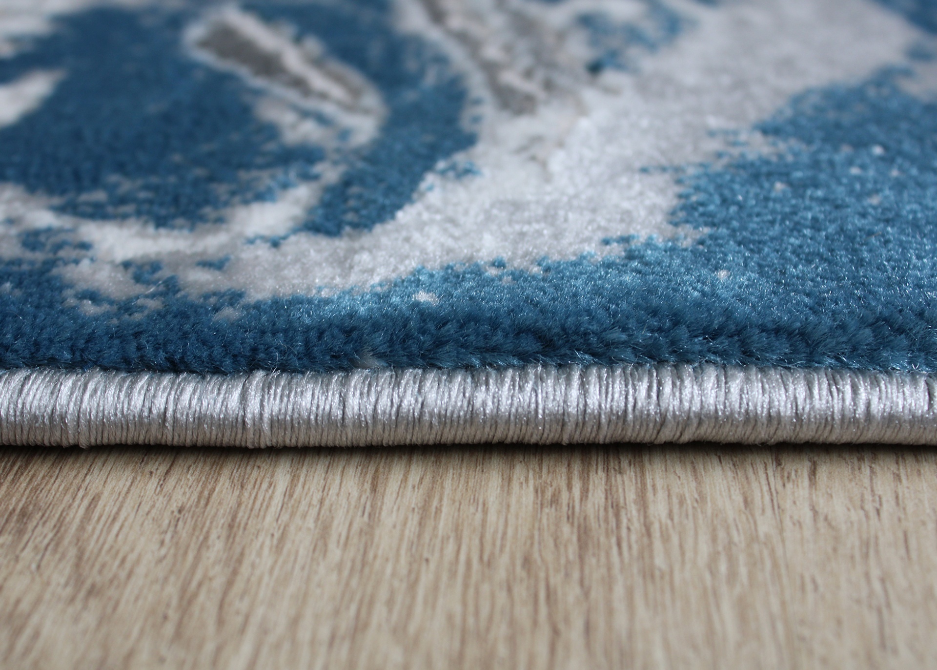 tapete azul e cinza com borda cinza prateada sobre piso de madeira clara