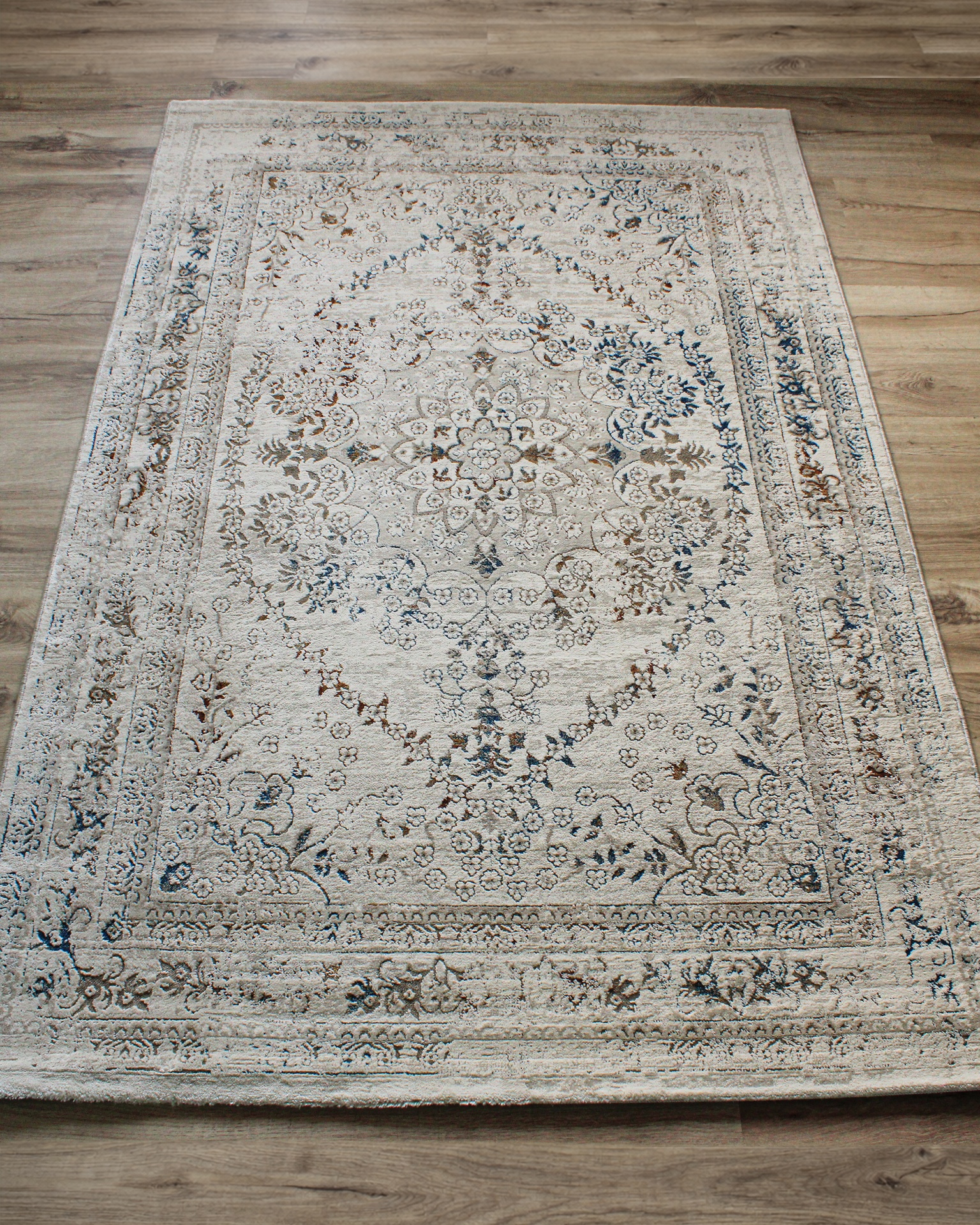 Tapete retangular com padrão floral intricado em tons de bege, azul e castanho sobre chão de madeira.