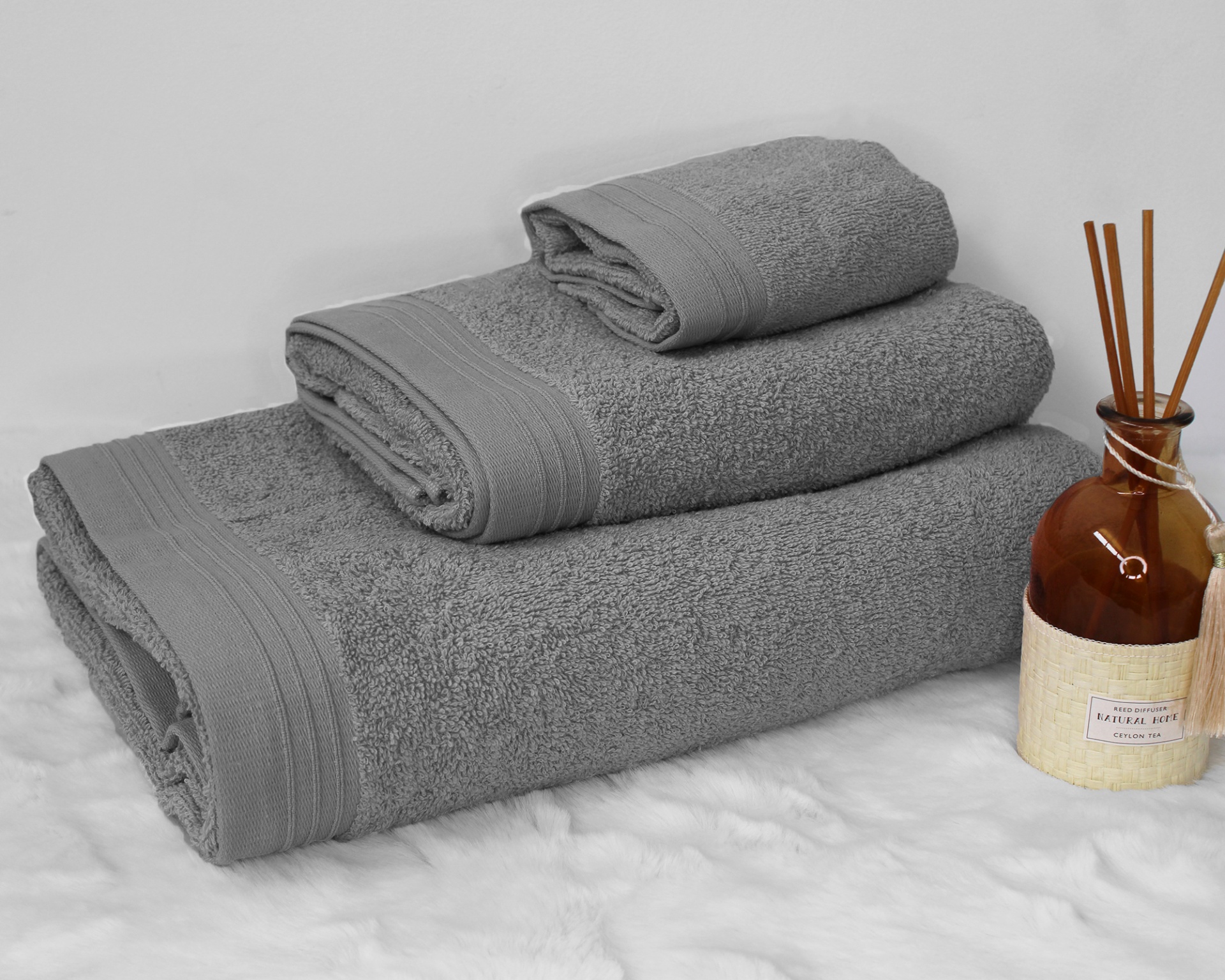 Três toalhas cinzentas empilhadas ao lado de frasco com difusor