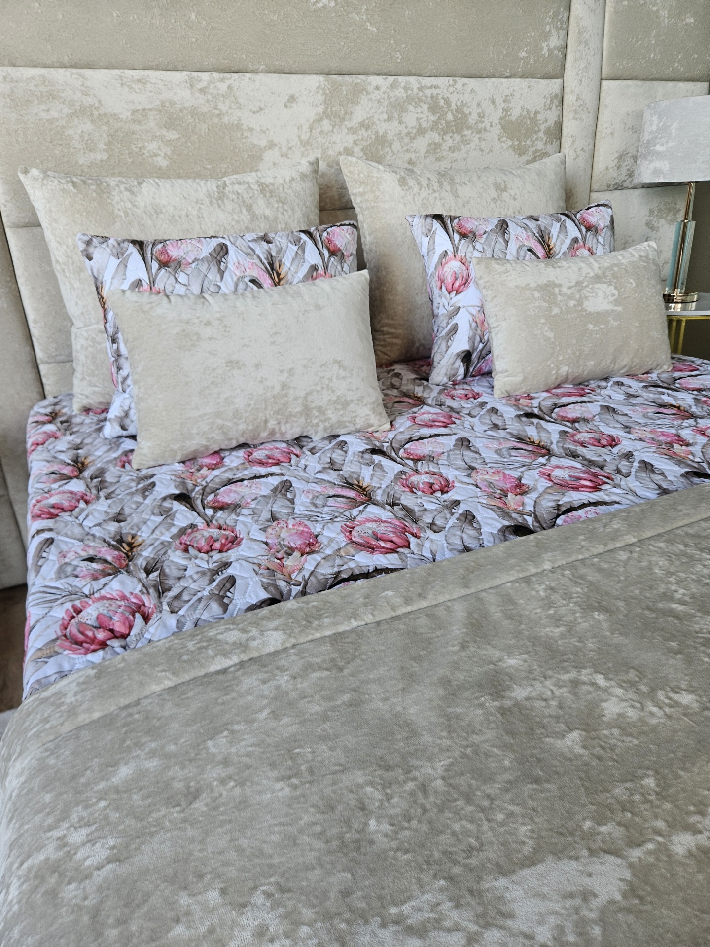Roupa de cama com padrão floral e almofadas de veludo bege em cama com cabeceira estofada bege