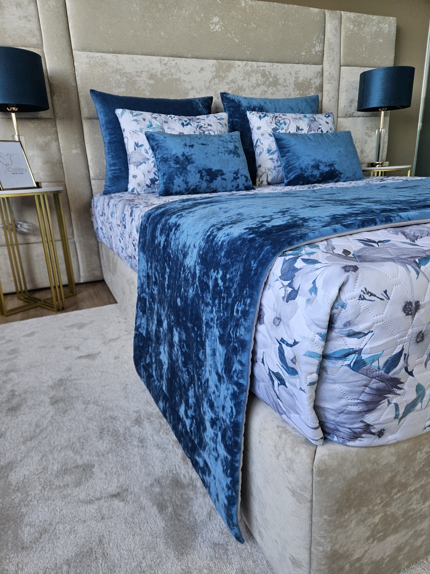 Cama estofada bege com roupa de cama floral azul e branca e almofadas azuis