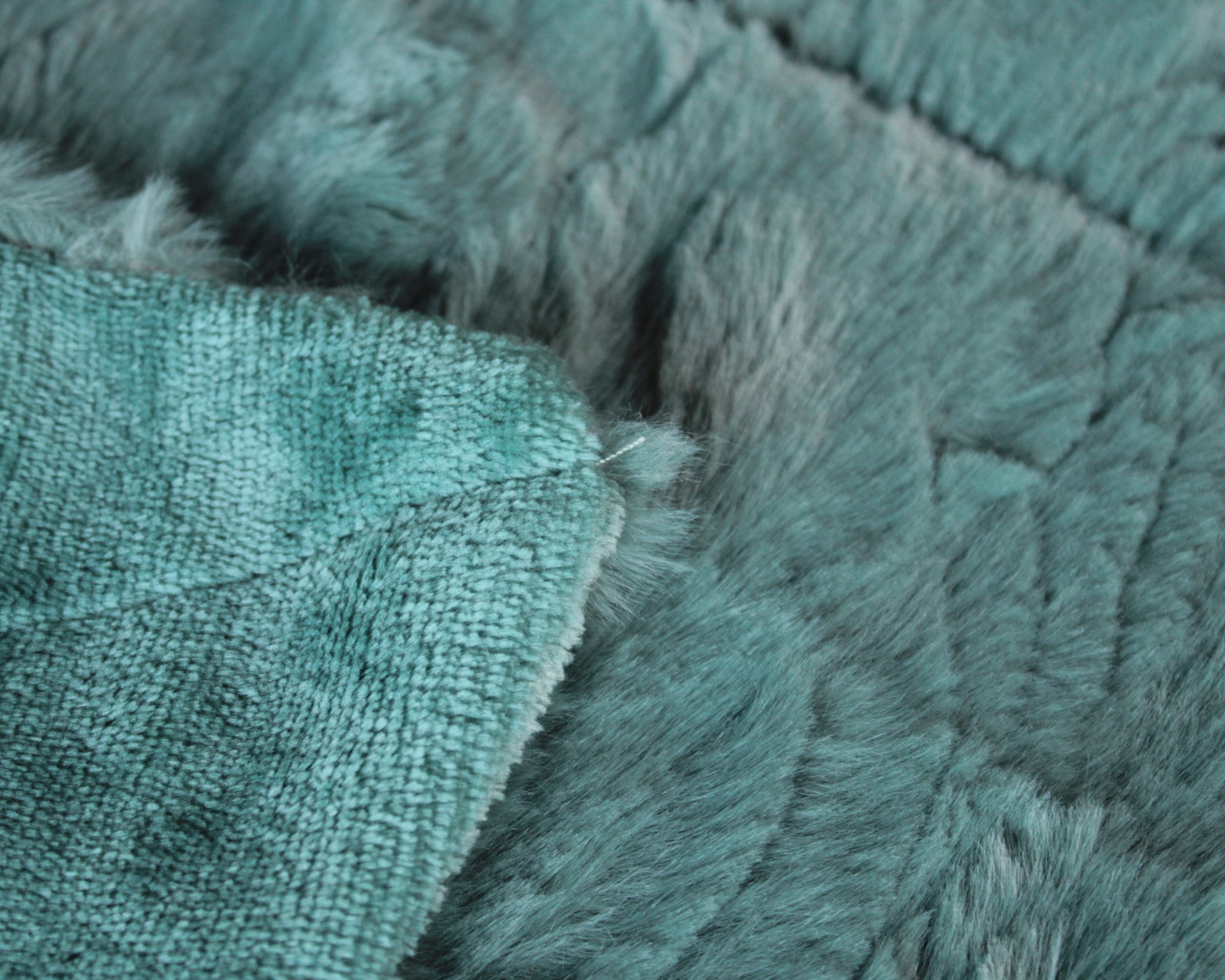 Tapete azul esverdeado com textura peluda e detalhe do tecido na parte de trás