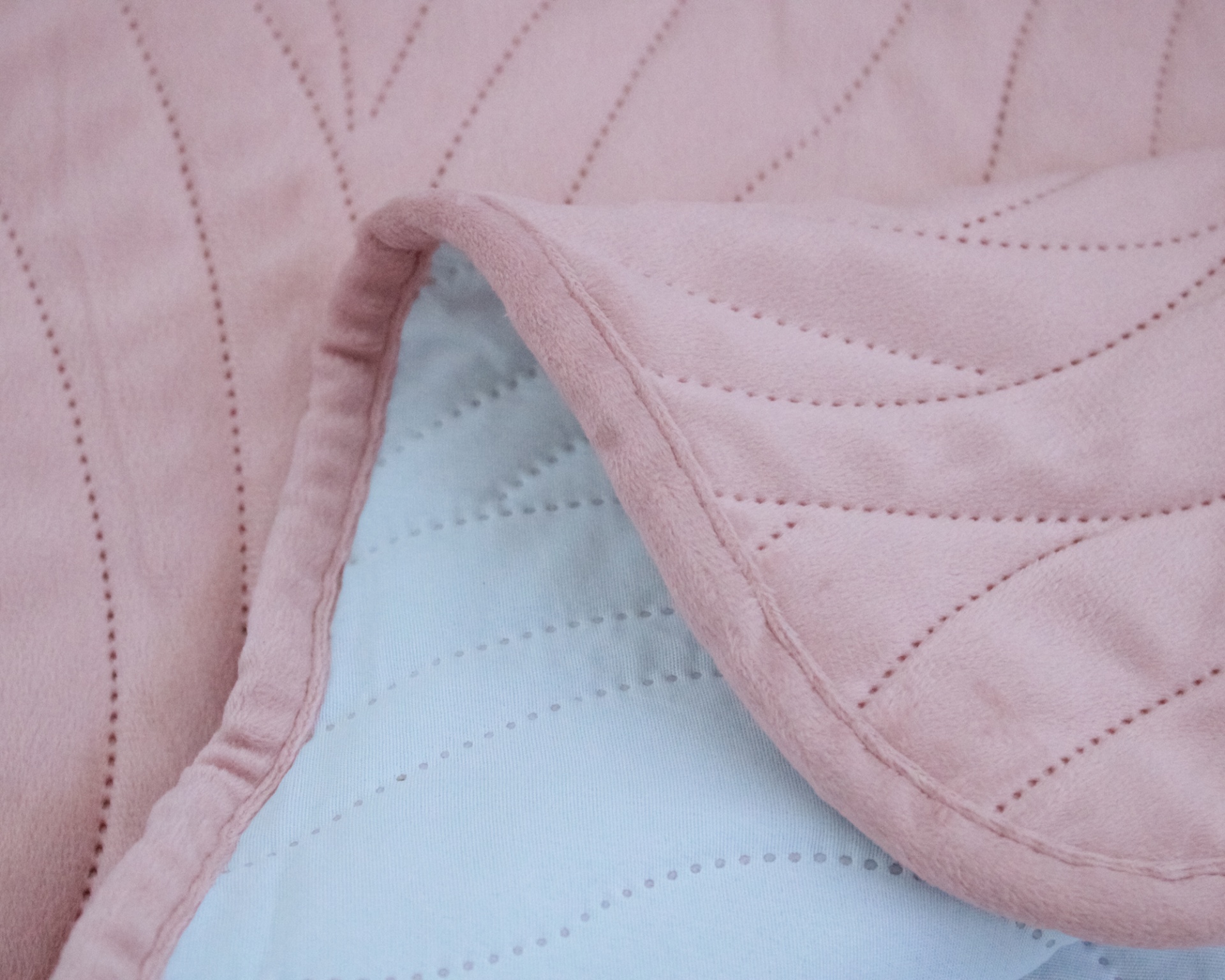 Colcha rosa claro com padrão de costura e reverso branco