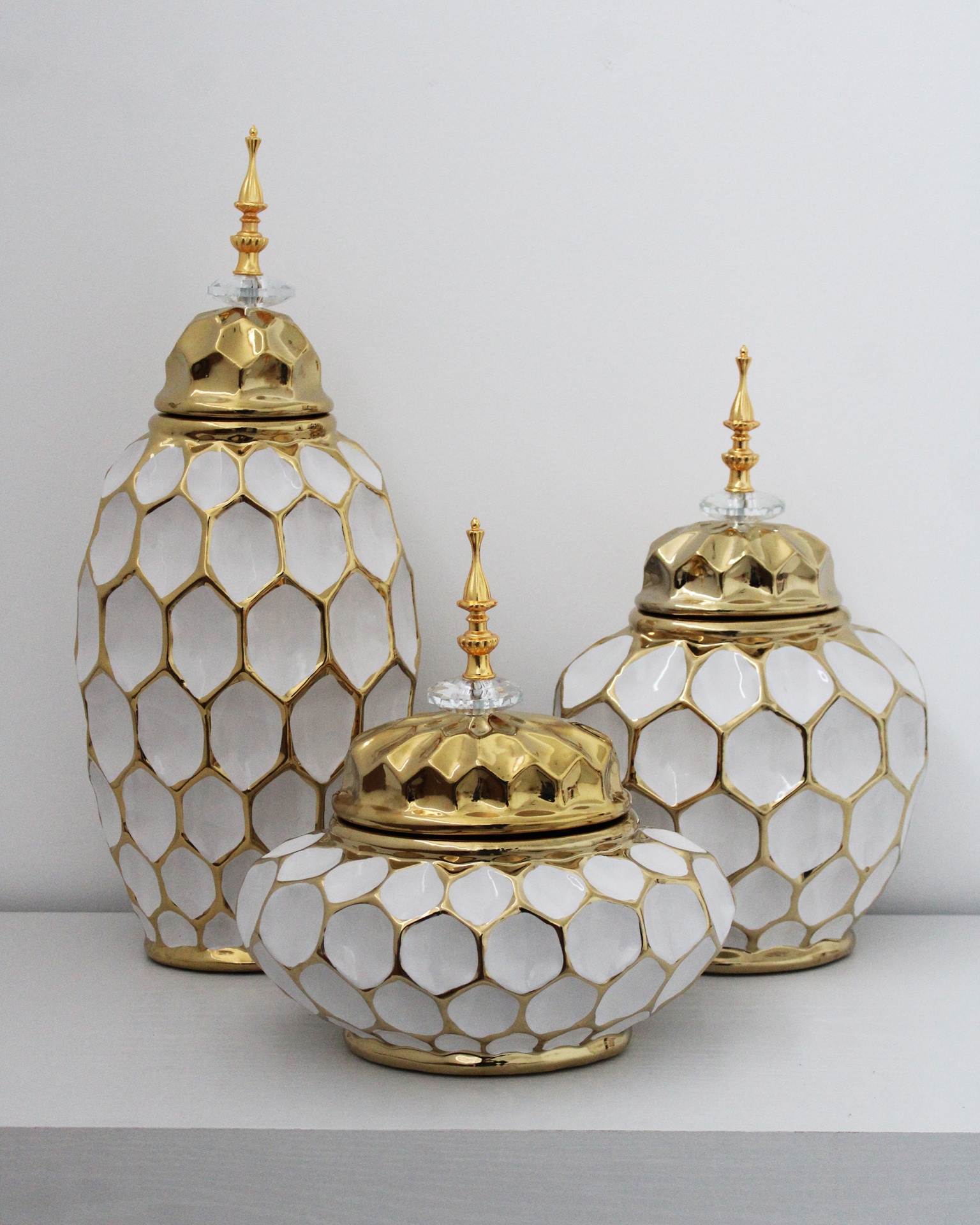 Três frascos decorativos dourados e brancos sobre superfície branca