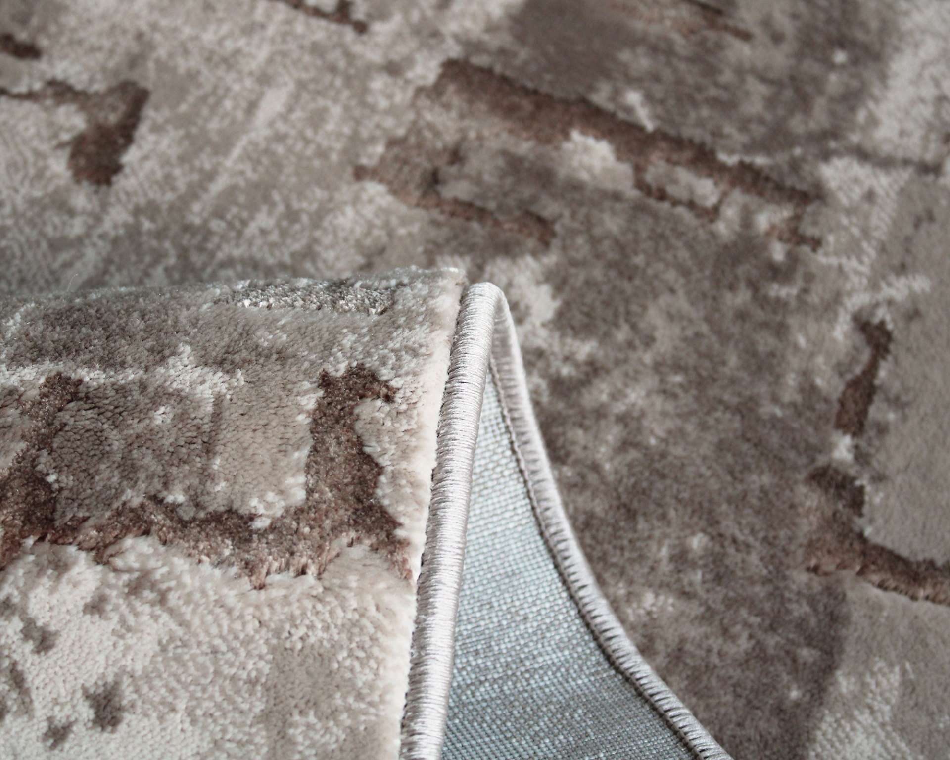 Tapete felpudo bege com padrão abstrato e bordas costuradas.