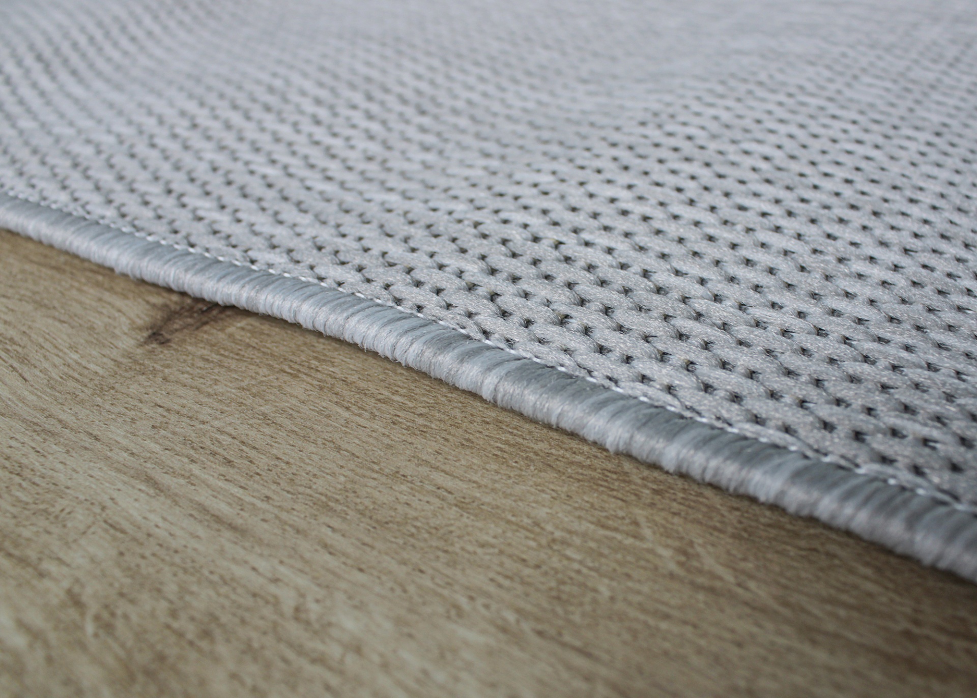 Borda de tapete cinza claro com textura em pequenos pontos sobre chão de madeira clara