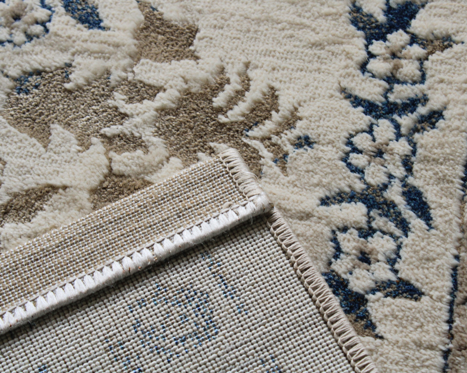 Tapete decorativo branco com padrão floral em azul e bege e bordas rematadas