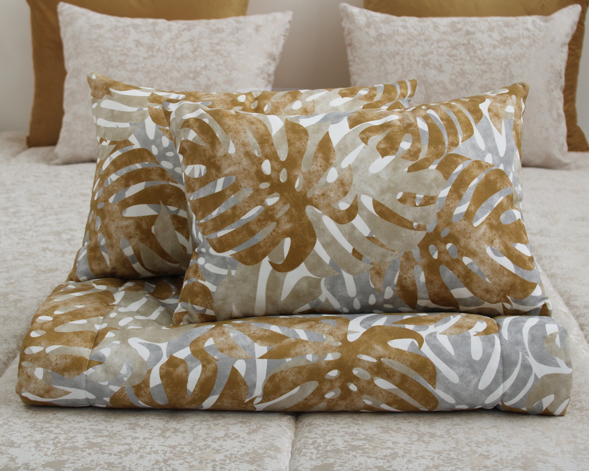 Conjunto de almofadas e edredão com padrão de folhas castanhas e cinzentas sobre cama bege