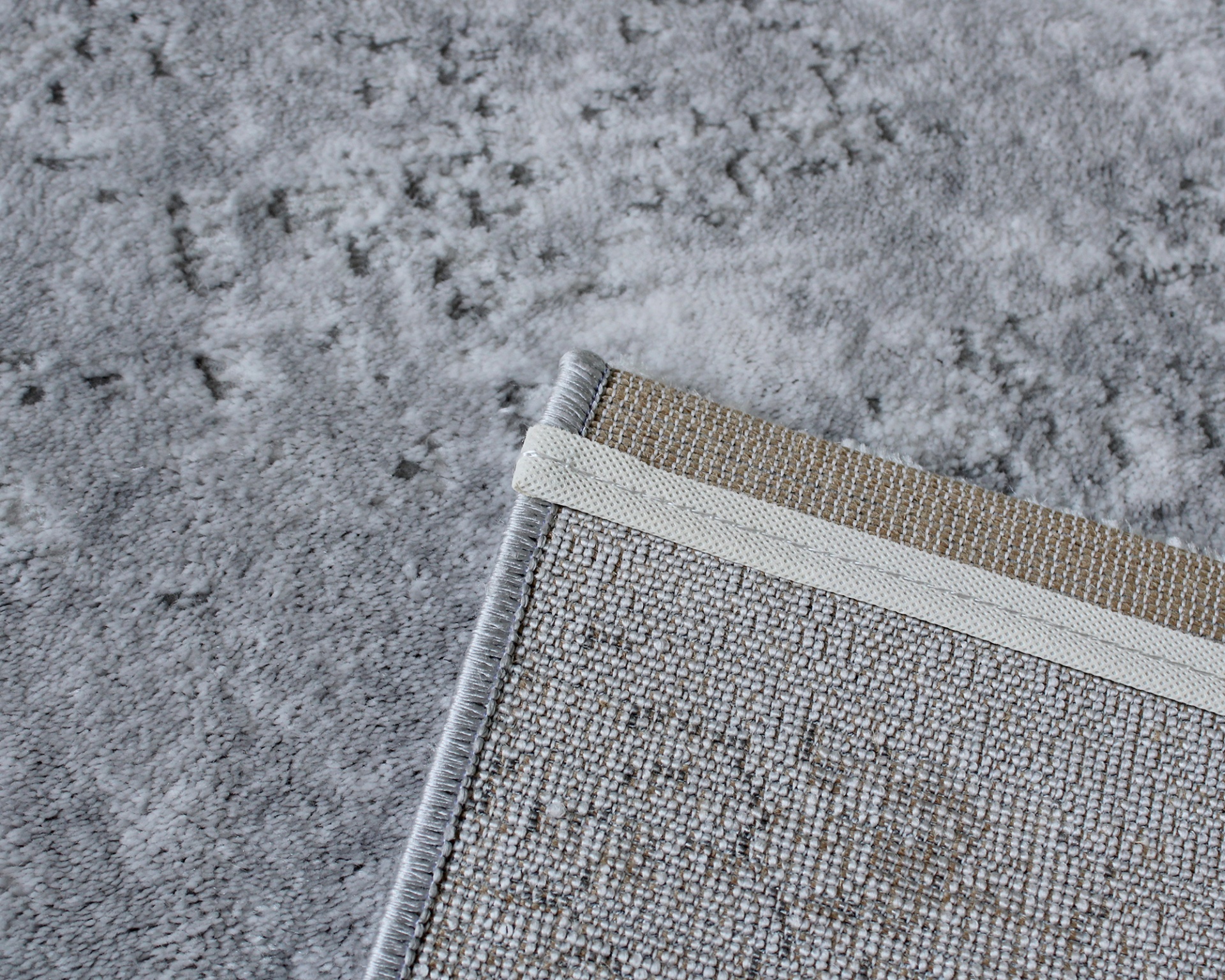 Canto de tapete cinza sobre tapete menor com trama e bordas costuradas