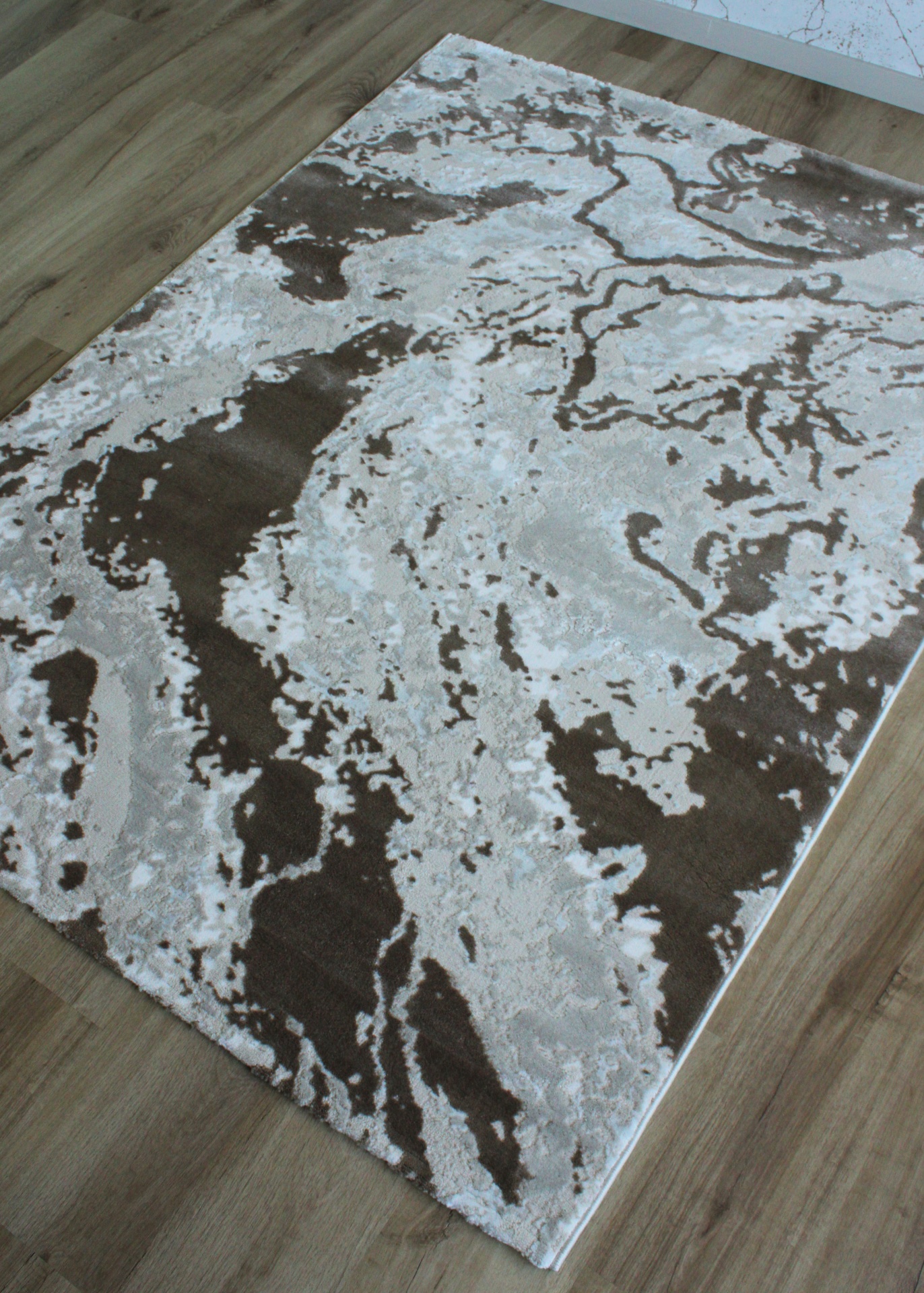 Tapete abstrato cinza, branco e castanho no chão de madeira.