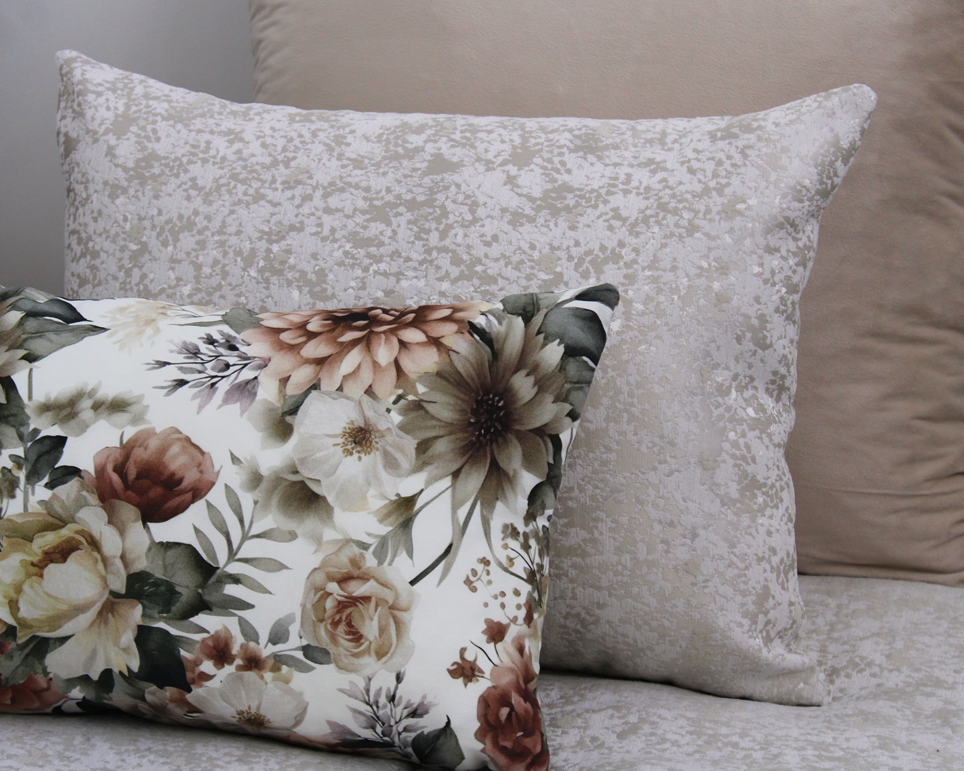 Três almofadas em tons de bege e floral sobre sofá ou cama