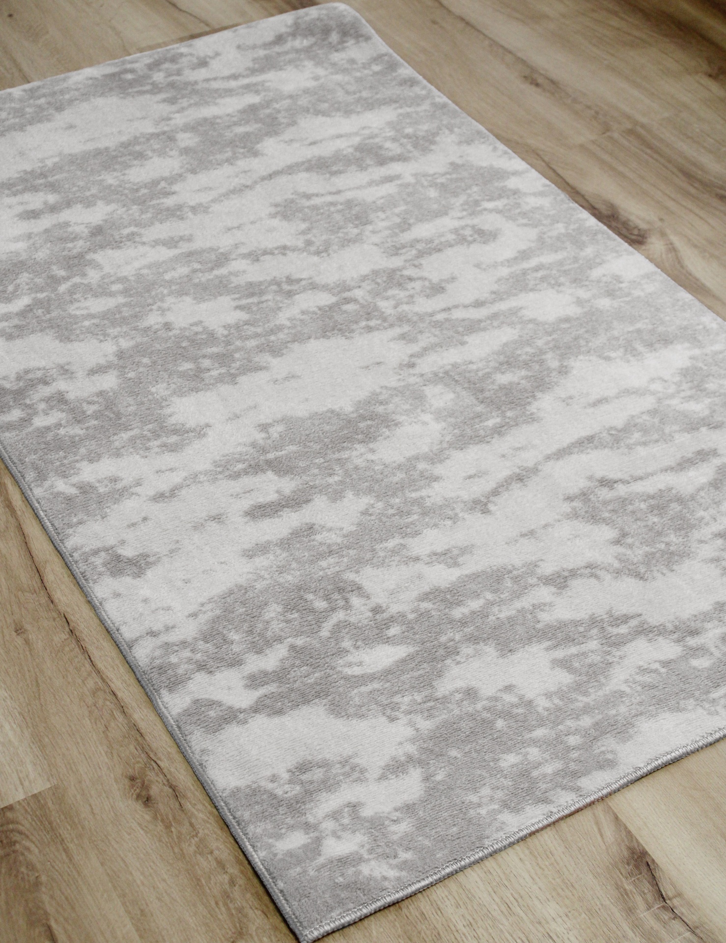 Tapete rectangular cinza claro e branco sobre chão de madeira clara
